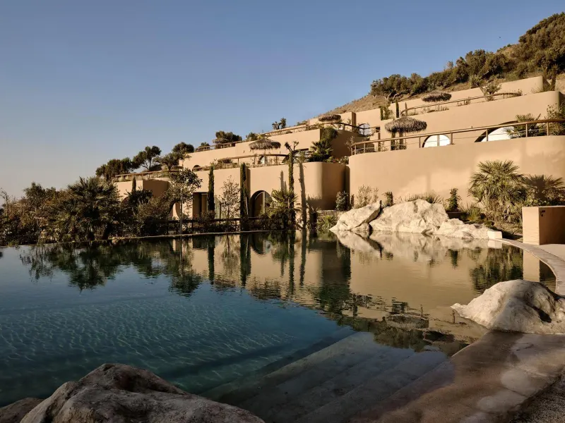 Hillside hotel buildings reflected in pool at dusk