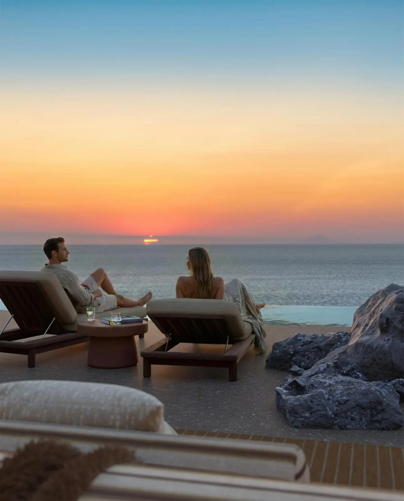 Couple watching sunset from loungers by infinity pool