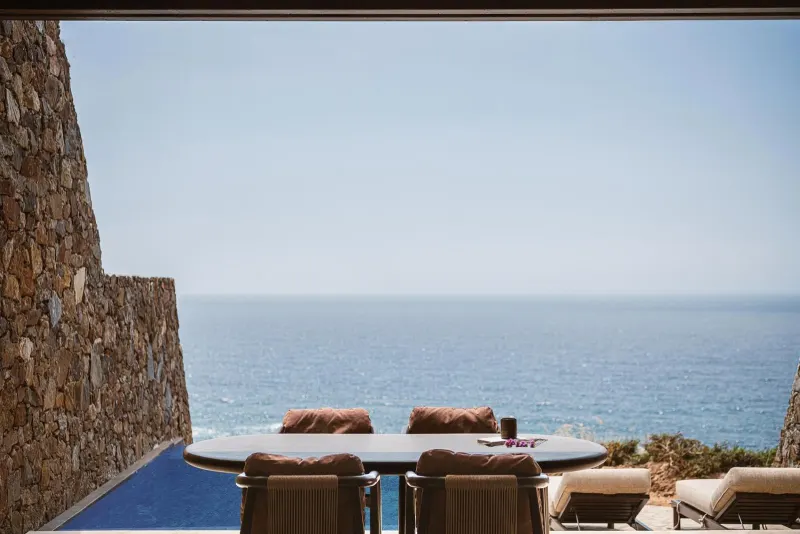 Outdoor dining table framed by stone wall and sea