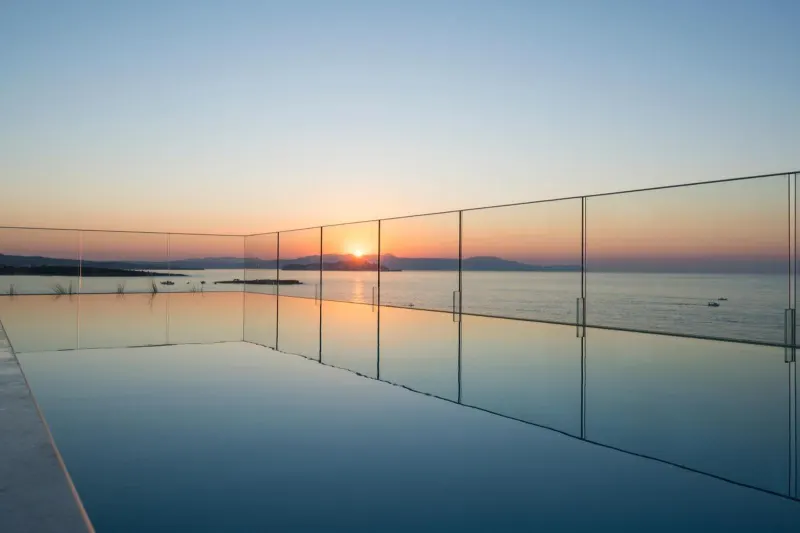Glass-edged pool reflecting sunset over the sea