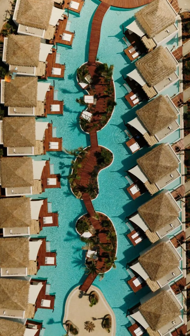 Aerial view symmetrical pool with thatched bungalows