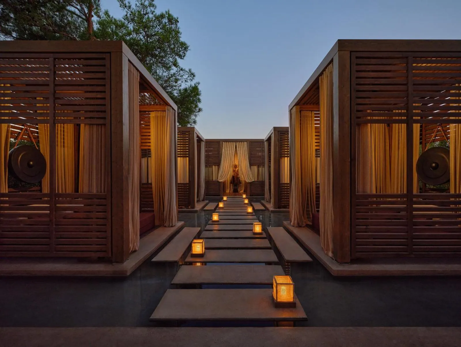 Wooden spa cabanas lit at dusk along stone path