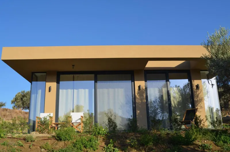 Modern glass-walled bungalow exterior with terrace chairs