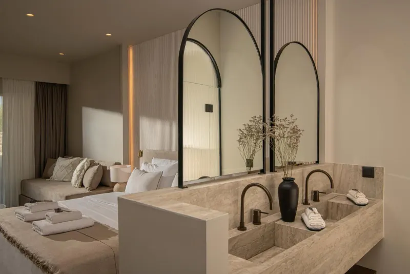 Bathroom vanity with arched mirrors and bedroom view
