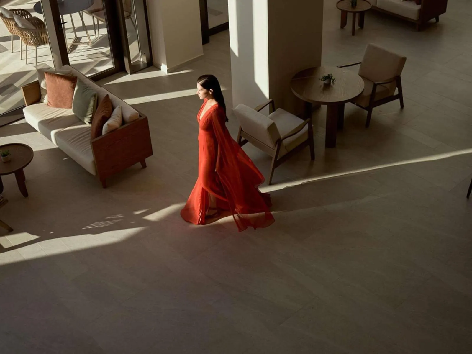 Woman in red dress walking through sunlit lobby